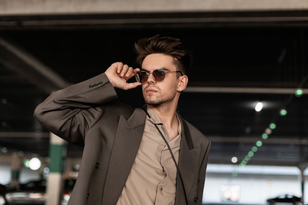 Handsome young business man with hairstyle in fashionable clothes look straightens sunglasses and walks on the street. Male casual style and fashion
