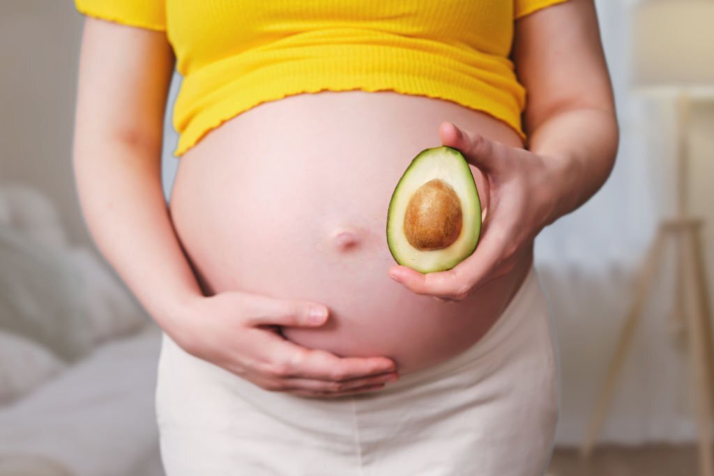 Avocado with a bone in the hands of a pregnant woman, home living room