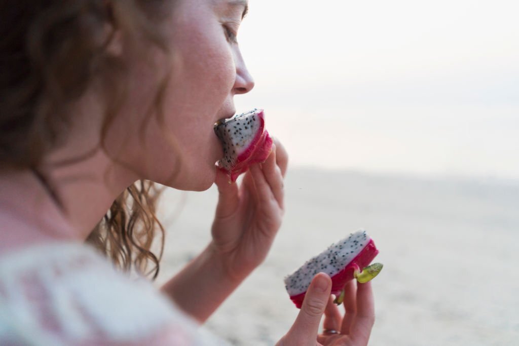 Close-up shot of a young caucasian woman eating dragon fruit on the beach.