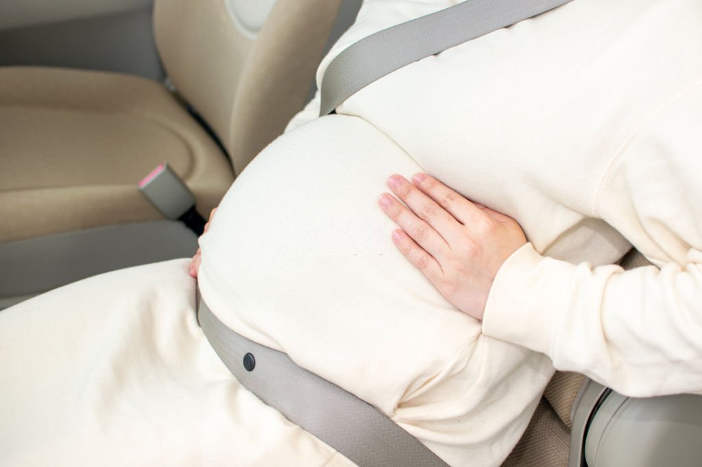 A young pregnant Asian woman wears a seatbel at a passenger seat and gets ready to visit a hospital