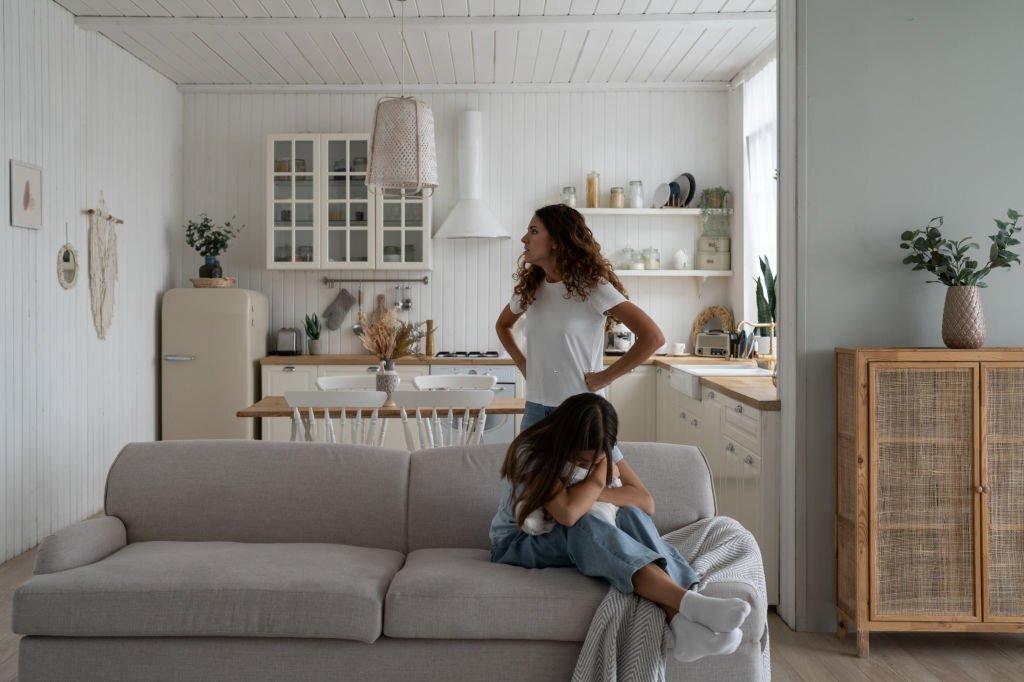 Toxic mother verbally abusing child, arguing with kid at home, sad depressed girl daughter sitting on sofa hugging pillow and crying while mom scolding her. Difficult mother-daughter relationship