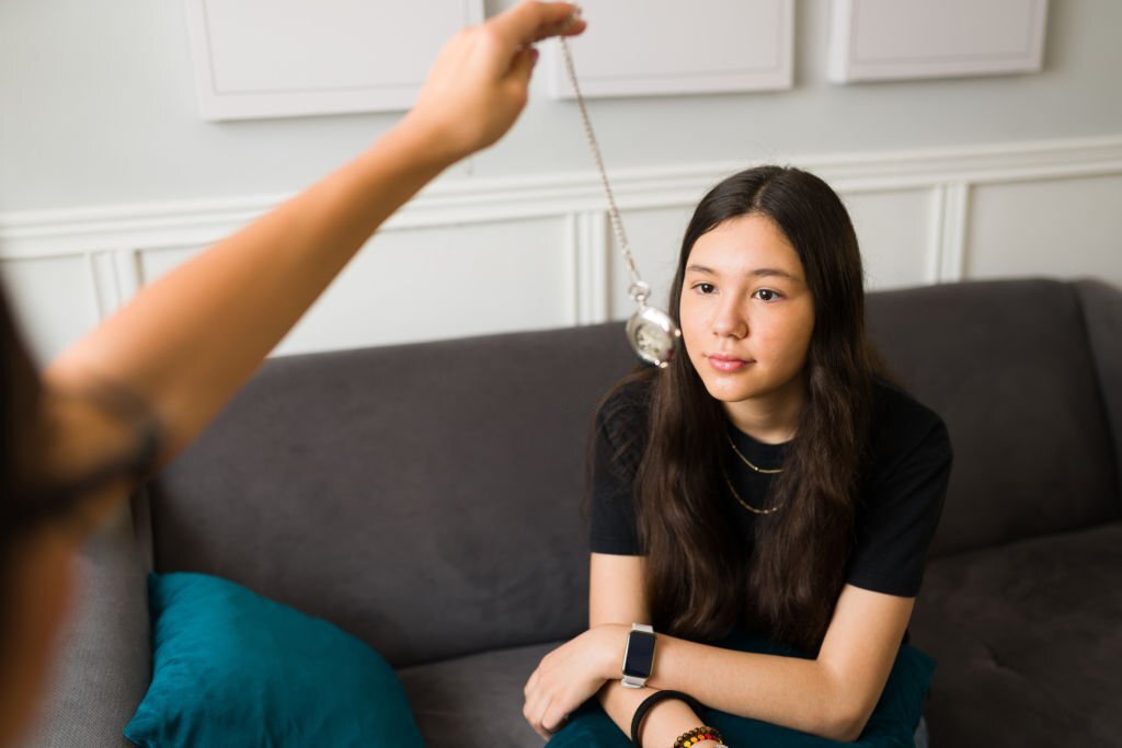 Caucasian teenage girl looking at a clock to get hypnotized during a therapy session. Therapist hand using a clock to hypnotize a teen patient