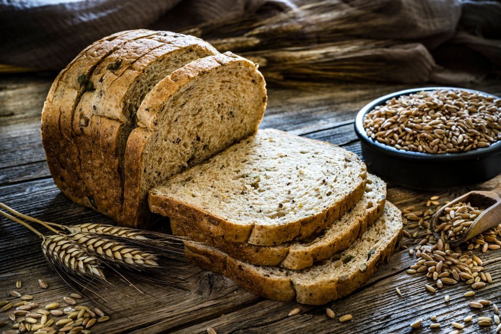 Wholegrain sliced bread shot on rustic wooden table. A bowl filled with wholegrain spelt is at the right beside the sliced bread. XXXL 42Mp studio photo taken with SONY A7rII and Zeiss Batis 40mm F2.0 CF