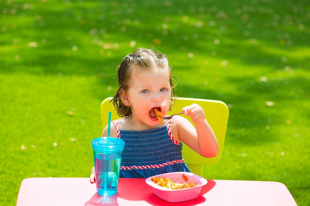 Toddler kid girl eating macaroni tomato pasta in garden turf grass