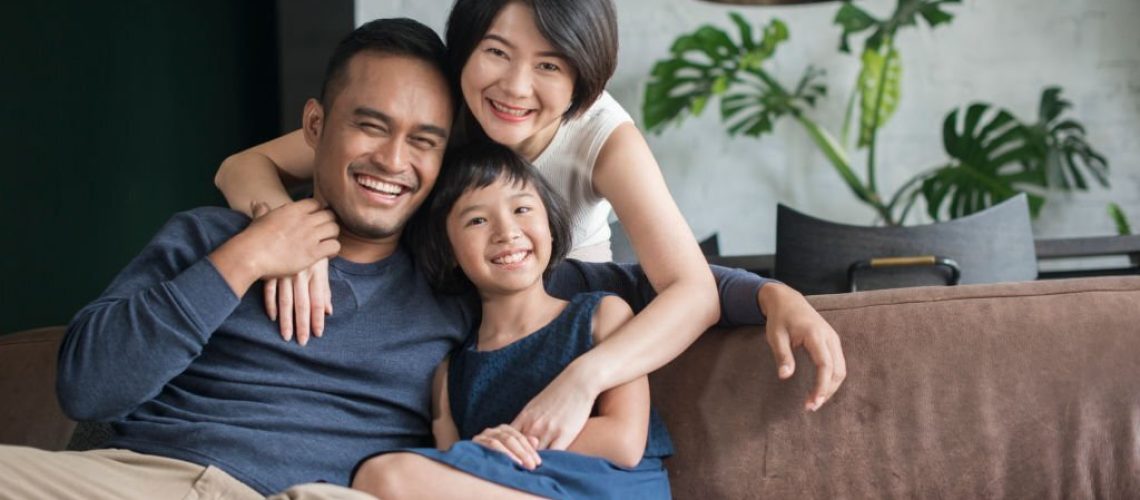 Young Asian parents with only child relaxing on the sofa in the living room.