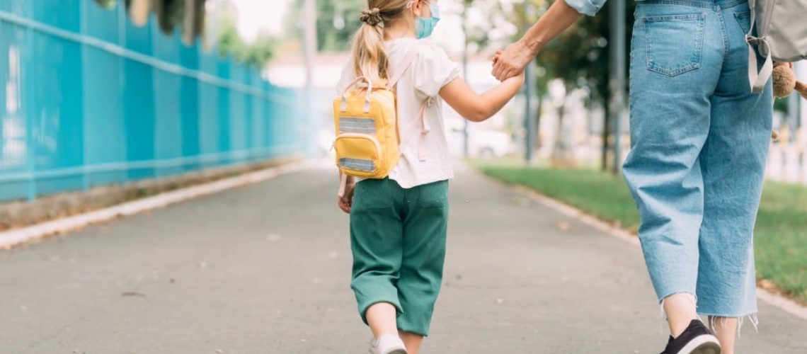 Virus prevention: a cute girl wearing a protective face masks goes to school with her mother.