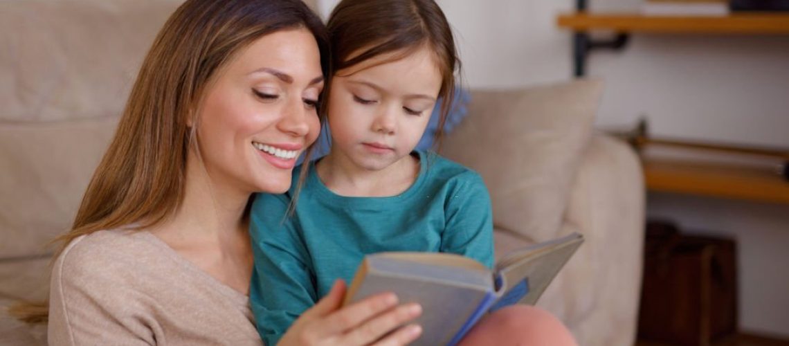 Happy mother and daughter reading book together at home