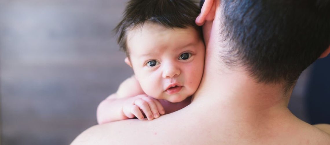 Newborn baby and dad. Father with baby looking over his shoulder. The child is looking at the camera