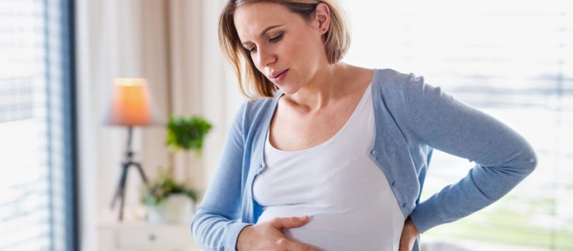 A portrait of pregnant young woman indoors at home, feeling tired.