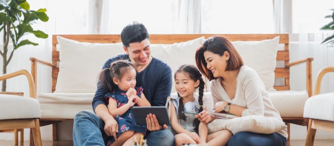 Happy Asian family using tablet, laptop for playing game watching movies, relaxing at home for lifestyle concept