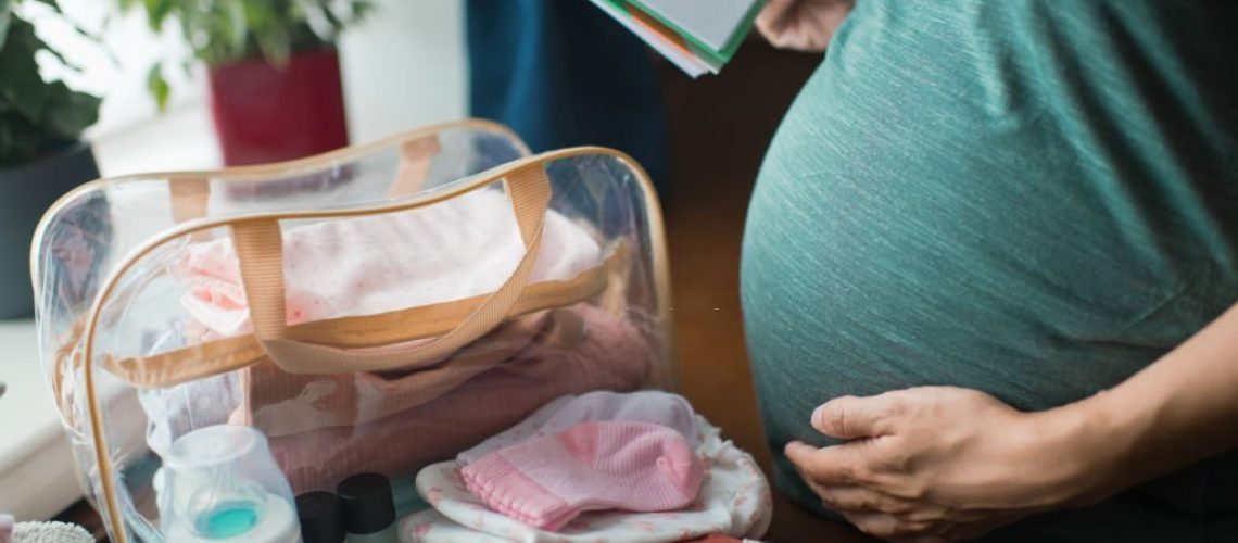 Pregnant woman at home preparing bag for newborn baby