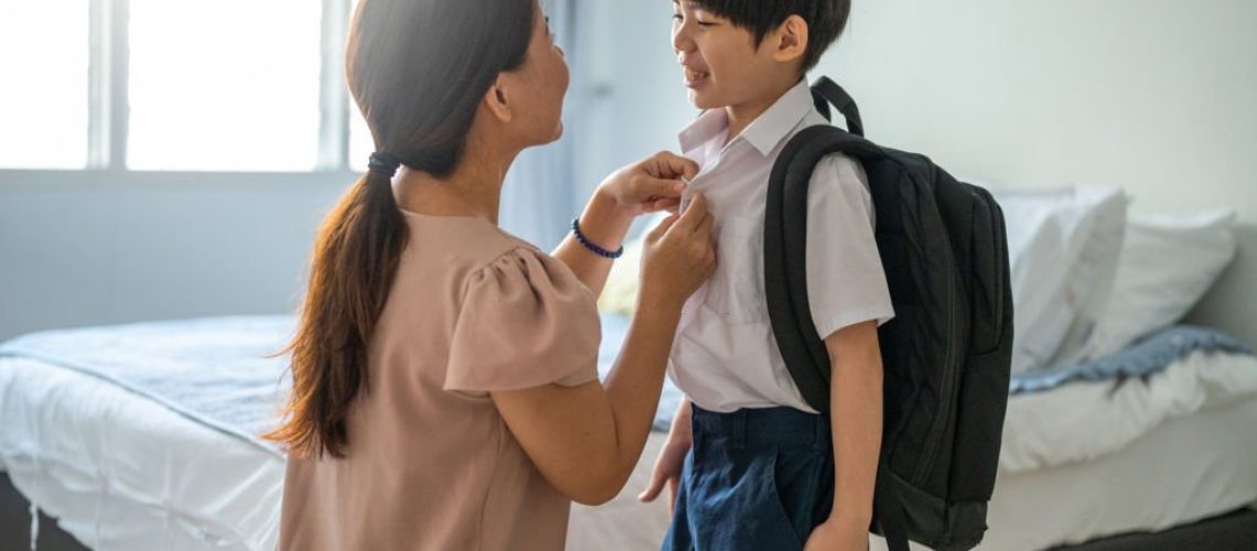 An Asian mother getting her son ready for school at home.