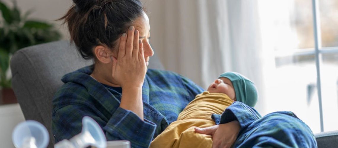 Tired mother holding her newborn child at home after tying to pump.