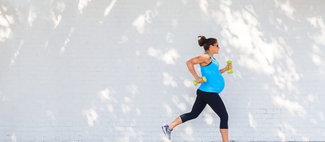 Young pregnant woman jogging down sidewalk in city.