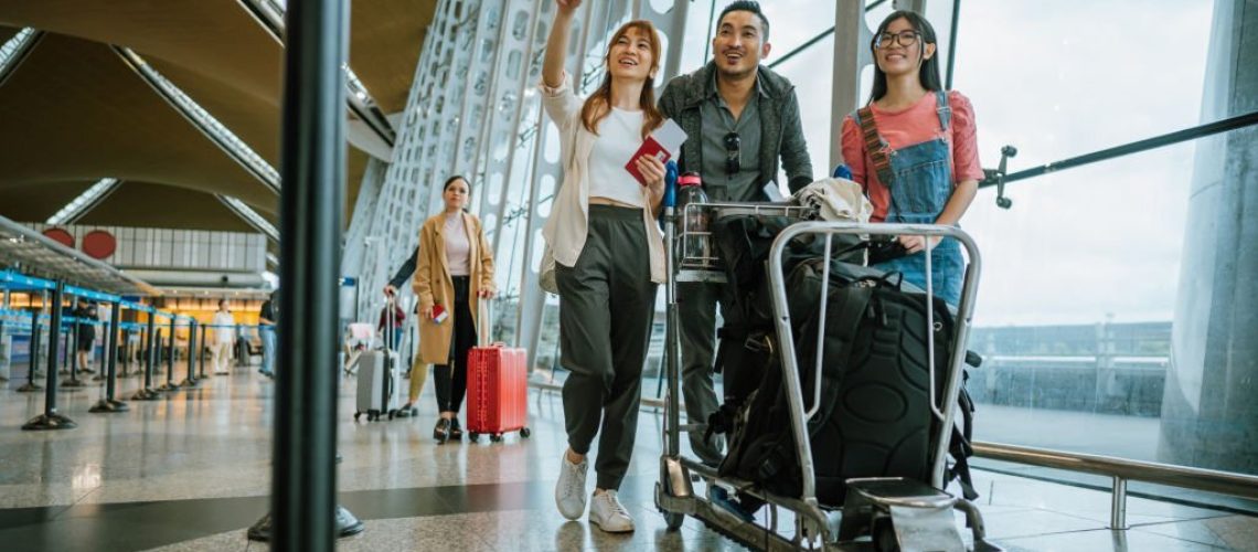 Asian Chinese family with young daughter arrival at airport. Tourist family at airport terminal with their luggage on trolley.