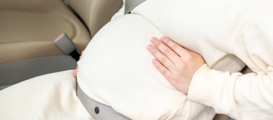 A young pregnant Asian woman wears a seatbel at a passenger seat and gets ready to visit a hospital