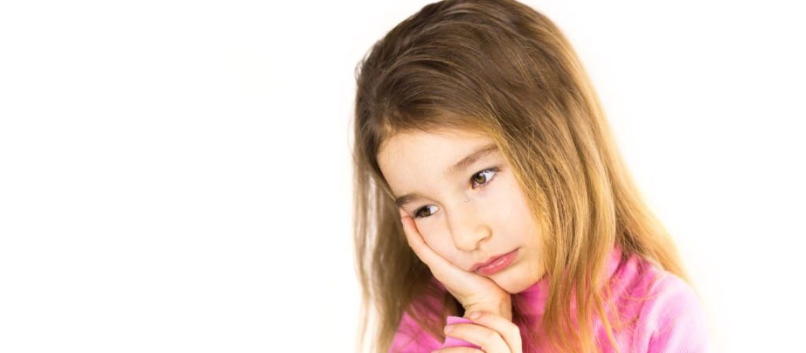 Little girl with sad face holds her cheek with hand - tooth hurts. Ear pain, toothache, swollen cheek and gums, problems of pediatric dentistry. Child medicine. Sadness and expectation. Isolated