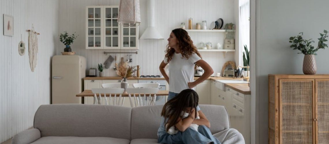 Toxic mother verbally abusing child, arguing with kid at home, sad depressed girl daughter sitting on sofa hugging pillow and crying while mom scolding her. Difficult mother-daughter relationship