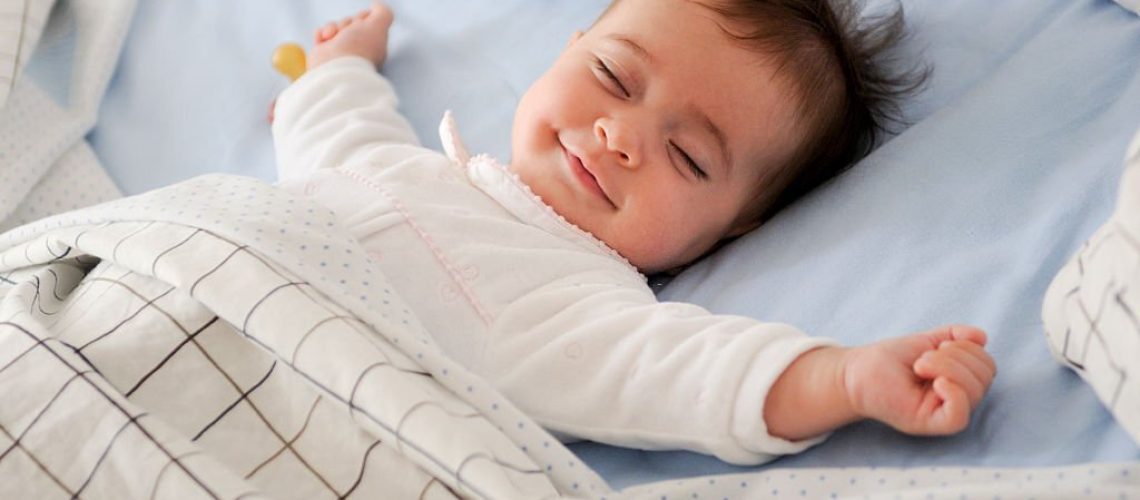 Smiling baby girl lying on a bed sleeping and smiling on blue sheets
